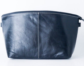 May include: A black leather zippered pouch with white stitching. The pouch is made of a soft, textured leather.