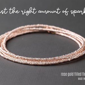 Puede incluir: Un delicado collar de oro rosa hecho de pequeñas cuentas. El collar está en capas y tiene un brillo sutil. El texto "rose gold filled findings" y "MADE IN USA" es visible debajo del collar.