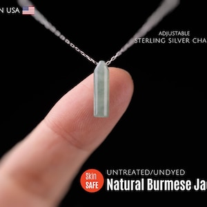 May include: A light green, rectangular pendant made of Natural Burmese Jade, suspended from an adjustable sterling silver chain. The necklace is displayed against a black background. The text "MADE IN USA" is visible.