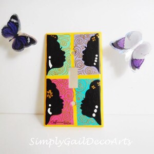 Könnte beinhalten: Ein Lichtschalter-Abdeckung mit einem farbenfrohen Design mit vier schwarzen Silhouetten von Frauen. Der Hintergrund ist eine Mischung aus Türkis, Rosa und Gelb mit goldenen Akzenten. Die Schalterabdeckung ist mit "Gail 2020" signiert.