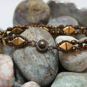 May include: A brown and gold beaded bracelet with a magnetic clasp. The bracelet is made with small, faceted beads and features a geometric pattern.