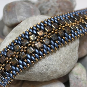 Pode incluir: Um bracelete de contas com um padrão geométrico em tons de azul e marrom.