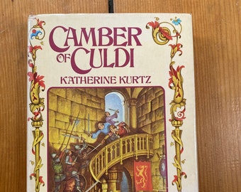 May include: A book cover with a yellow background and a red and gold border. The title is "Camber of Culdi" by Katherine Kurtz. The cover art depicts a scene of a castle interior with a spiral staircase and several people in medieval clothing.