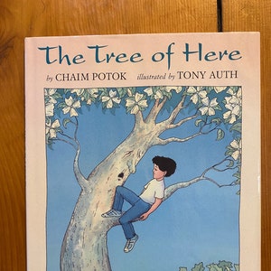 May include: A book titled "The Tree of Here" by Chaim Potok, illustrated by Tony Auth. The cover features a colorful illustration of a boy sitting in a tree with white flowers.