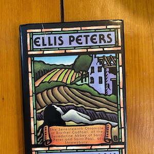 Könnte beinhalten: Ein Buch mit dem Titel "The Potter's Field" von Ellis Peters. Das Cover zeigt eine farbenfrohe Illustration einer Landschaft mit Feldern, einem Gebäude und Text in einem Rahmen im Stil eines Glasfensters.