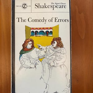 May include: A vintage paperback book cover featuring a black and white illustration of two people in a yellow and blue setting. The book title is "The Comedy of Errors" by Shakespeare. The Signet Classic logo is in the top right corner.
