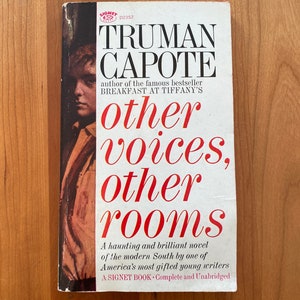 May include: A white book cover with red text that reads "TRUMAN CAPOTE" and "other voices, other rooms". The book is by the author of "Breakfast at Tiffany's".