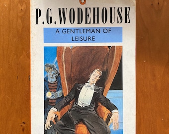 May include: A Penguin Books paperback cover featuring a cartoon illustration of a man in a tuxedo lying back in a chair with a surprised expression. A man with a flashlight stands behind the chair. The book title is "A Gentleman of Leisure" by P.G. Wodehouse.