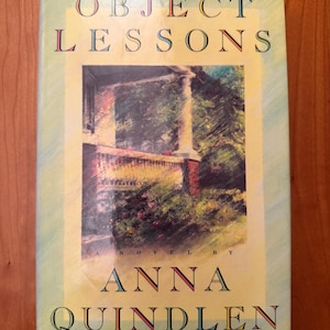 May include: A paperback book titled "Object Lessons" by Anna Quindlen. The cover features a watercolor painting of a porch with trees and a light yellow background. The title and author's name are in a serif font.