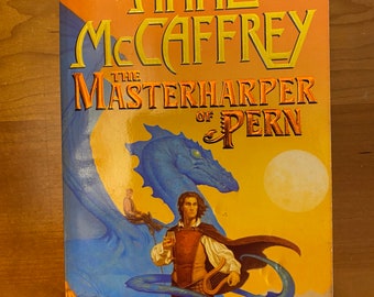 以下が含まれることがあります： 青いドラゴンとライダー、ハープを持った男性、そして「Anne McCaffrey The Masterharper of Pern」というテキストが書かれた本の表紙。背景は白っぽい月のある黄色がかったオレンジ色の夕焼けです。