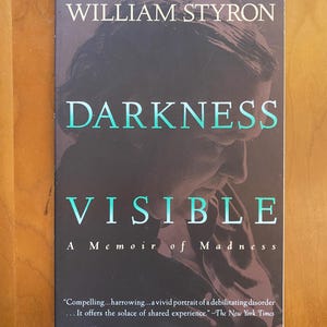 May include: A hardcover book titled "Darkness Visible" by William Styron. The cover is dark with teal lettering and a portrait of a person. The book is a memoir about madness and is a #1 national bestseller.