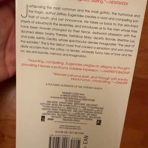 Op de afbeelding: Achterkant van het boek "The Virgin Suicides", met citaten en credits. De titel en auteur zijn zichtbaar, evenals het ISBN en de prijs. De achtergrond is wit met zwarte tekst.