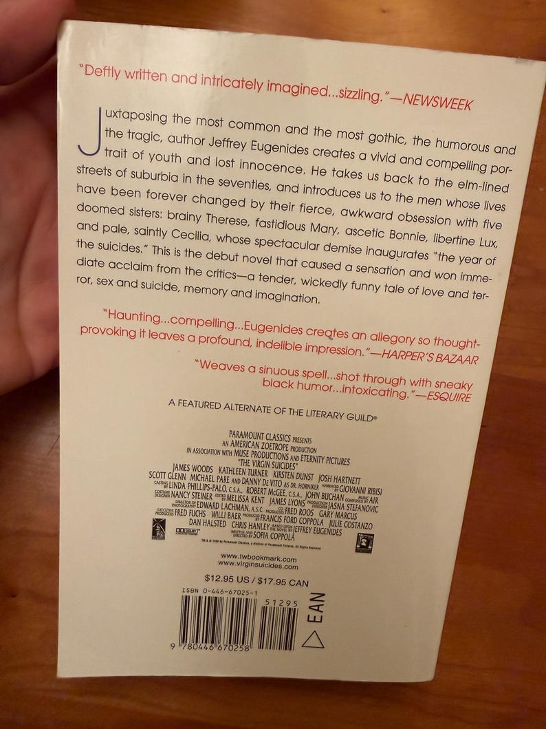 Op de afbeelding: Achterkant van het boek "The Virgin Suicides", met citaten en credits. De titel en auteur zijn zichtbaar, evenals het ISBN en de prijs. De achtergrond is wit met zwarte tekst.