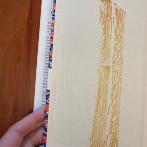 May include: A vintage book with a cream cover and a decorative red, white, and blue patterned edge. The spine has a faded brown design. The book's pages are visible, and the text is partially legible.
