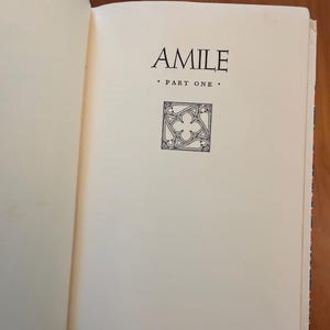 May include: An open book showing the title "AMILE" in black serif font. Below the title is "PART ONE" and a decorative square graphic. The pages are off-white.