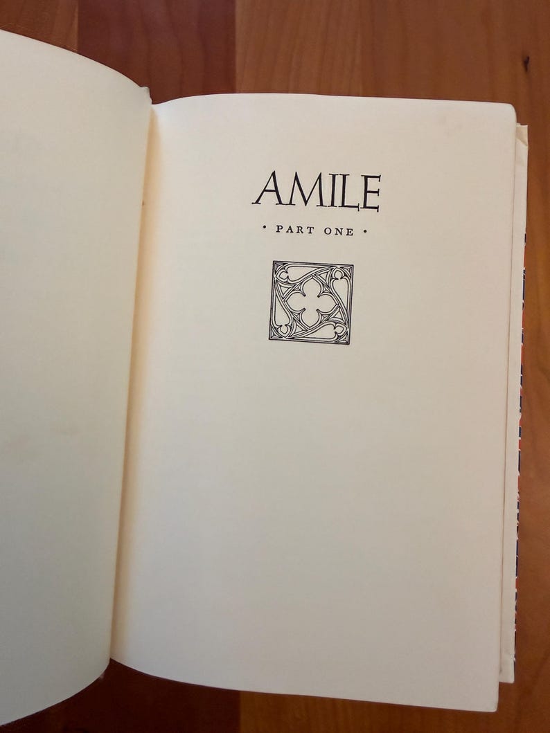 May include: An open book showing the title "AMILE" in black serif font. Below the title is "PART ONE" and a decorative square graphic. The pages are off-white.