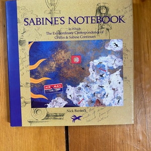 May include: A brown book with a blue spine titled "Sabine's Notebook: In Which The Extraordinary Correspondence of Griffin & Sabine Continues". The cover features a colorful illustration of a map with a red arrow, a sun, and a blue and white "AIR MAIL" stamp.