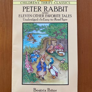 Może przedstawiać: Vintage książka "Peter Rabbit and Eleven Other Favorite Tales" autorstwa Beatrix Potter. Okładka przedstawia kolorową ilustrację Petera Królika i innych postaci zwierzęcych w scenerii ogrodu. Książka należy do serii Dover Children's Thrift Classics.