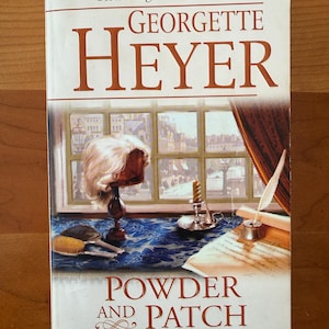 May include: A paperback book titled "Powder and Patch" by Georgette Heyer. The cover features a window scene with a wig, candle, and quill. The book has a white background with brown and red text.
