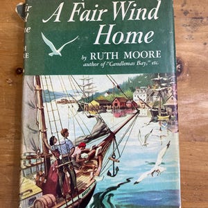 May include: A vintage hardcover book, "A Fair Wind Home" by Ruth Moore. The cover is green with white text and a seagull illustration. The book's cover art shows a sailing ship with people on board, sailing on blue water, with a harbor in the background.