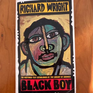Op de afbeelding: Boekomslag van "Black Boy" van Richard Wright. De cover toont een kleurrijk, gestileerd portret tegen een zwarte achtergrond. De titel staat in rode letters, de naam van de auteur in geel.