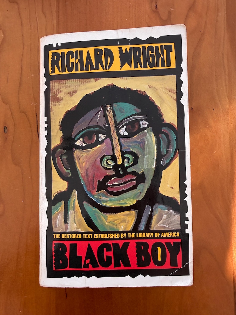 Op de afbeelding: Boekomslag van "Black Boy" van Richard Wright. De cover toont een kleurrijk, gestileerd portret tegen een zwarte achtergrond. De titel staat in rode letters, de naam van de auteur in geel.