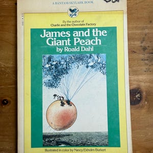 May include: A vintage paperback book titled "James and the Giant Peach" by Roald Dahl. The cover features a large peach illustration with characters and the text "A BANTAM-SKYLARK BOOK". The book is illustrated in color by Nancy Ekholm Burkert.