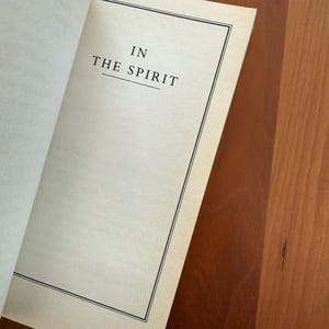 K&ouml;nnte beinhalten: Offenes Buch mit dem Text "IN THE SPIRIT" zentriert auf der Seite. Der Text ist in einer Serifenschrift, und die Seite hat einen schwarzen Rahmen. Das Buch liegt auf einer Holzoberfl&auml;che.