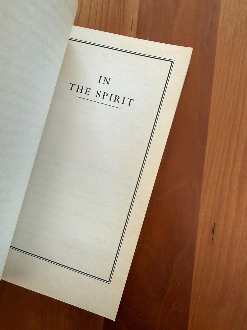 K&ouml;nnte beinhalten: Offenes Buch mit dem Text "IN THE SPIRIT" zentriert auf der Seite. Der Text ist in einer Serifenschrift, und die Seite hat einen schwarzen Rahmen. Das Buch liegt auf einer Holzoberfl&auml;che.