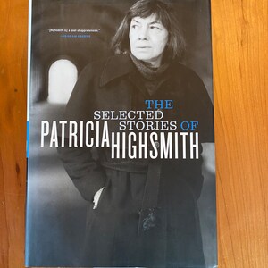 May include: A black and white photo of Patricia Highsmith on the cover of a book titled "The Selected Stories of Patricia Highsmith". A quote from Graham Greene is printed above the title: "[Highsmith is] a poet of apprehension."