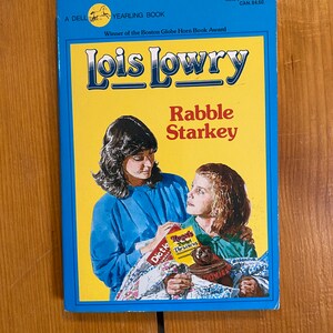 May include: A blue and yellow paperback book cover with the title "Rabble Starkey" by Lois Lowry. The book is a Yearling Book and a winner of the Boston Globe Horn Book Award.
