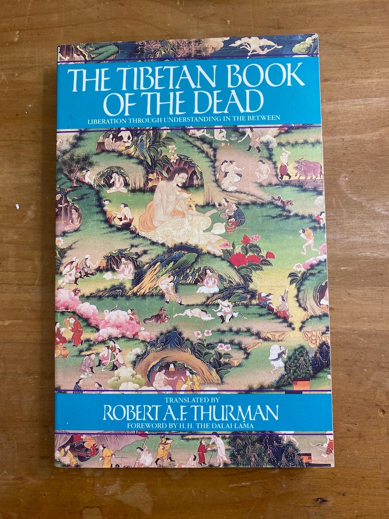 Puede incluir: El Libro Tibetano de los Muertos: Liberaci&oacute;n a trav&eacute;s de la comprensi&oacute;n en el intermedio, traducido por Robert A.F. Thurman con un pr&oacute;logo de S.S. el Dalai Lama. La portada presenta una ilustraci&oacute;n colorida de una escena pac&iacute;fica con muchas figuras.