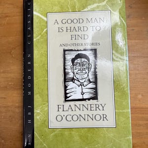 May include: A hardcover book titled "A Good Man Is Hard to Find and Other Stories" by Flannery O'Connor. The book has a green cover with white text and a black and white portrait. The spine reads "HBJ Modern Classic".