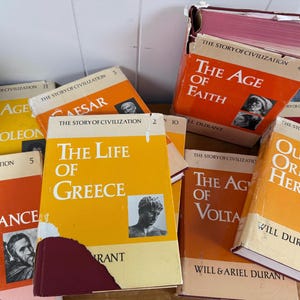Op de afbeelding: Een verzameling hardcover boeken met oranje, gele en rode covers. Titels zijn onder meer "The Age of Faith", "The Life of Greece" en "Our Oriental Heritage". De boeken maken deel uit van de serie "The Story of Civilization".