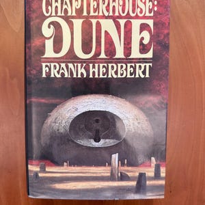 May include: A hardcover book titled "CHAPTERHOUSE: DUNE" by Frank Herbert. The cover features a large, spherical structure with a keyhole-like opening, set against a reddish-brown background. The title is in large, white, stylized letters.