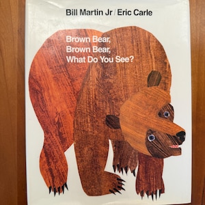 以下が含まれることがあります： ビル・マーティンJr.とエリック・カールによる絵本「Brown Bear, Brown Bear, What Do You See?」の表紙。テクスチャ加工された大きな茶色のクマのイラストが白い背景に描かれています。