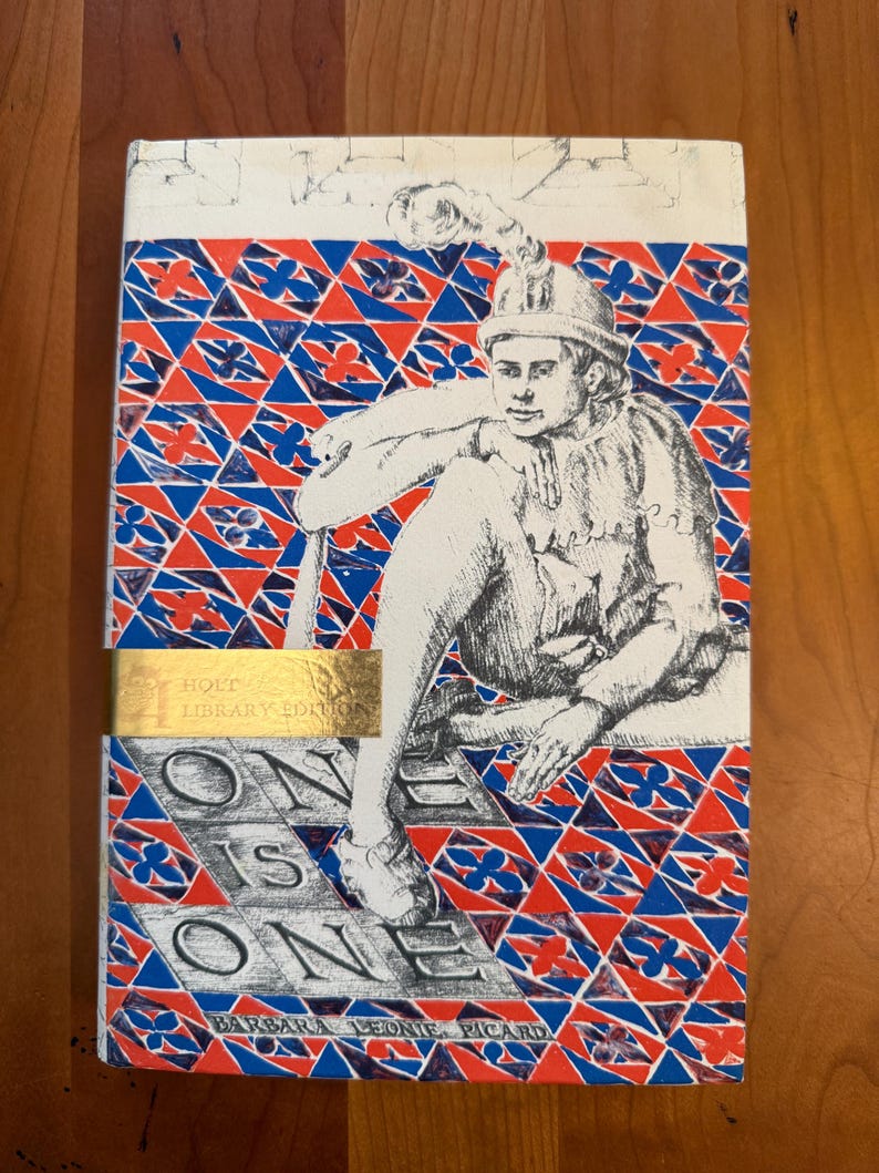 May include: A vintage hardcover book, "One is One" by Barbara Leonie Picard. The cover displays a detailed illustration of a person in historical clothing, set against a geometric pattern of red, blue, and white. The book has a gold label that reads "Holt Library Edition."