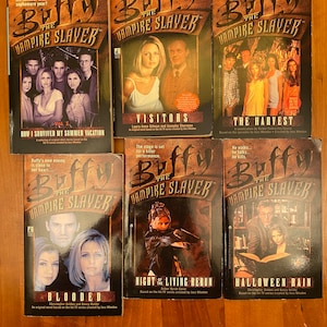 Könnte beinhalten: Sechs Taschenbücher aus der "Buffy the Vampire Slayer"-Reihe. Die Cover zeigen Bilder der Charaktere und Titel wie "Visitors" und "Halloween Rain". Die Bücher sind auf einer Holzoberfläche angeordnet.