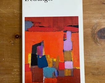 May include: A paperback book titled L'étranger by Albert Camus. The white cover features a rectangular graphic illustration composed of abstract blocks of colour in shades of bright orange, deep red, purple, blue, and black.