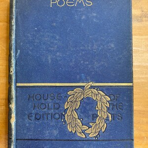 May include: A vintage hardcover book titled "Longfellow's Poems." The cover is a textured blue with gold lettering and a gold wreath design. The book is part of the "Household Edition of the Poets."