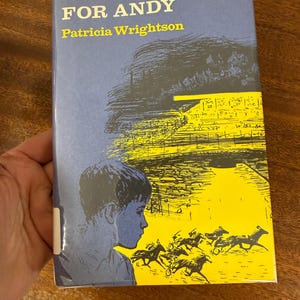 Puede incluir: Un libro titulado "A Racecourse for Andy" de Patricia Wrightson. La portada presenta un fondo azul con una ilustración amarilla y negra de un hipódromo y caballos. Una silueta de niño está en el lado izquierdo.