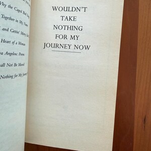 K&ouml;nnte beinhalten: Offene Buchseiten mit dem Text: "WOULDN'T TAKE NOTHING FOR MY JOURNEY NOW." Der Text ist auf der rechten Seite zentriert. Die linke Seite listet Buchtitel und Autorin Maya Angelou auf. Die Seiten sind cremefarben, vor einem Holzuntergrund.