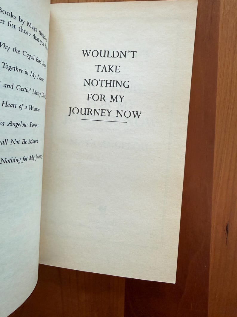 K&ouml;nnte beinhalten: Offene Buchseiten mit dem Text: "WOULDN'T TAKE NOTHING FOR MY JOURNEY NOW." Der Text ist auf der rechten Seite zentriert. Die linke Seite listet Buchtitel und Autorin Maya Angelou auf. Die Seiten sind cremefarben, vor einem Holzuntergrund.