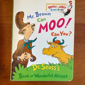 Op de afbeelding: Een kinderboek getiteld "Mr. Brown Can Moo! Can You?" van Dr. Seuss. De cover bevat illustraties van een man en een gele koe. Het boek is een "Bright and Early Board Book."