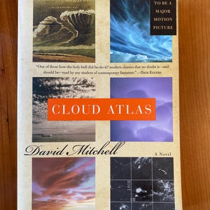 May include: A paperback book titled "Cloud Atlas" by David Mitchell. The cover features a collage of images, including cloud formations and a sunset. Text includes "New York Times Bestseller" and "Soon to be a Major Motion Picture."
