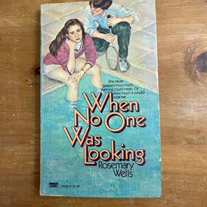 May include: A paperback book titled "When No One Was Looking" by Rosemary Wells. The cover features illustrations of two people near a pool, with text overlay. The book has a blue and pink color scheme.