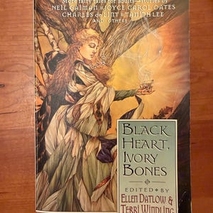 Pode incluir: Capa de livro com o título "Black Heart, Ivory Bones" apresentando uma ilustração de uma mulher segurando uma xícara com fumaça. A capa também inclui os nomes dos autores e editores.