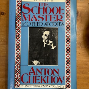 May include: A vintage book titled "The Tales of Chekhov, Volume 11." The cover is light blue with red and black decorative borders. The title "The Schoolmaster & Other Stories" is in large red letters. A black and white portrait of Anton Chekhov is featured.