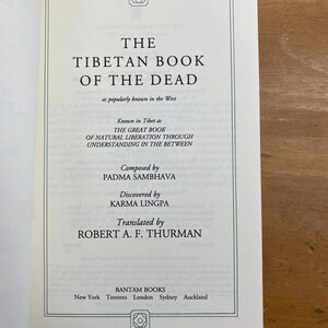 Puede incluir: El Libro Tibetano de los Muertos, una portada de libro con el t&iacute;tulo en texto negro sobre fondo blanco. El libro es conocido en el T&iacute;bet como "El Gran Libro de la Liberaci&oacute;n Natural a trav&eacute;s de la Comprensi&oacute;n en el Intermedio". Fue compuesto por Padma Sambhava y descubierto por Karma Lingpa. El libro fue traducido por Robert A.F. Thurman.