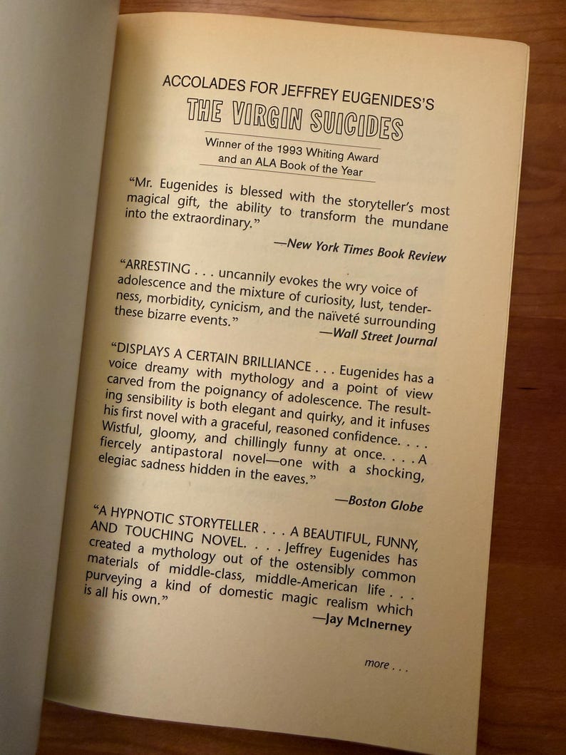 Op de afbeelding: Open boekpagina met de titel "THE VIRGIN SUICIDES" van Jeffrey Eugenides. Bevat recensies uit de New York Times, Wall Street Journal en Boston Globe. Winnaar van de Whiting Award 1993.